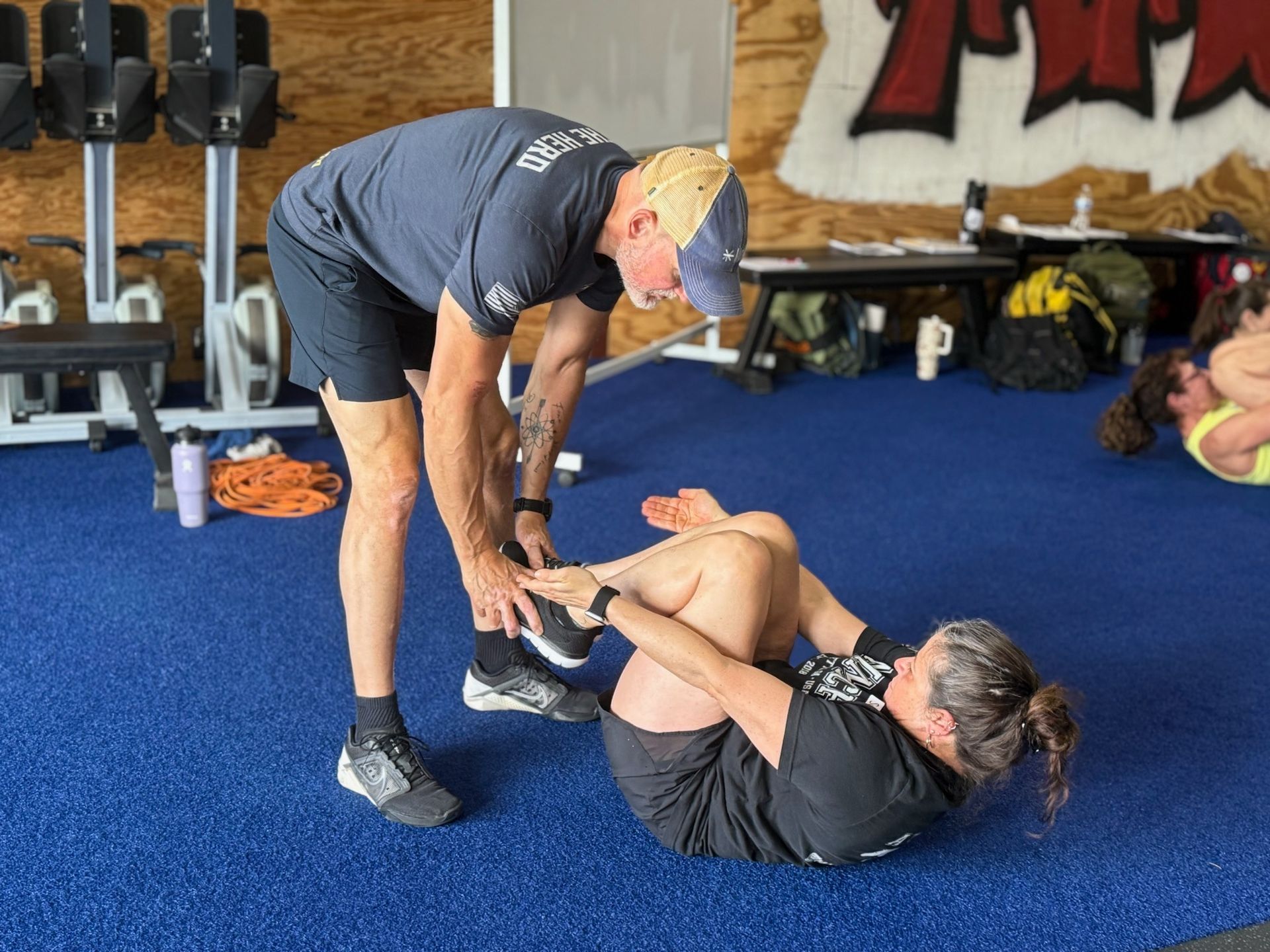 Trainer assisting person doing crunches on a blue floor in a gym.