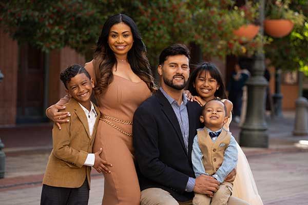 Family posing outdoors: woman in tan dress, man in blazer, with three children.