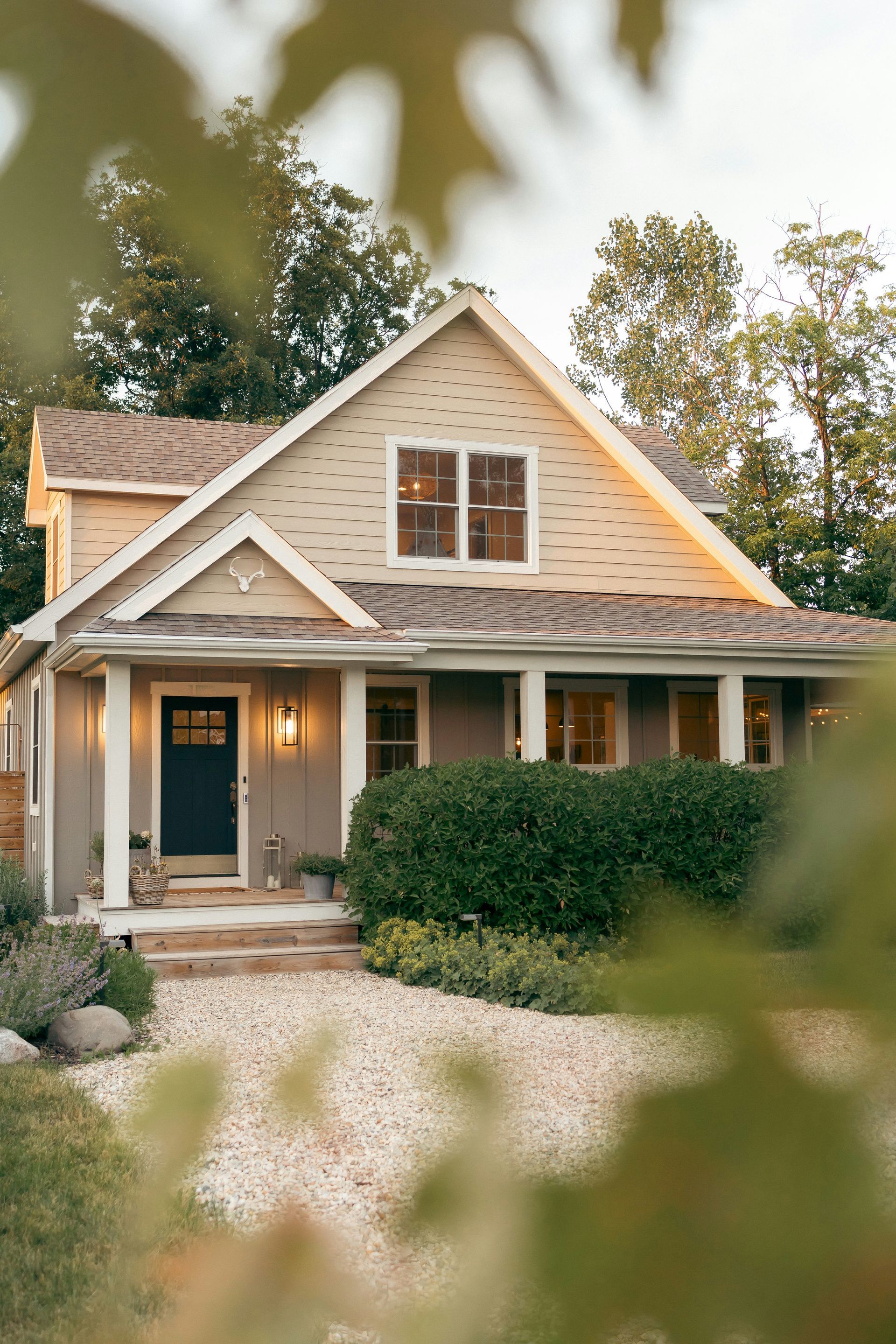 A house with a porch and a gravel driveway is surrounded by trees.