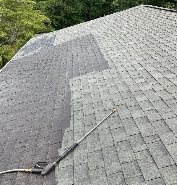 A black, rectangular chimney stands on a dark, tiled roof against a light blue, cloudy sky.