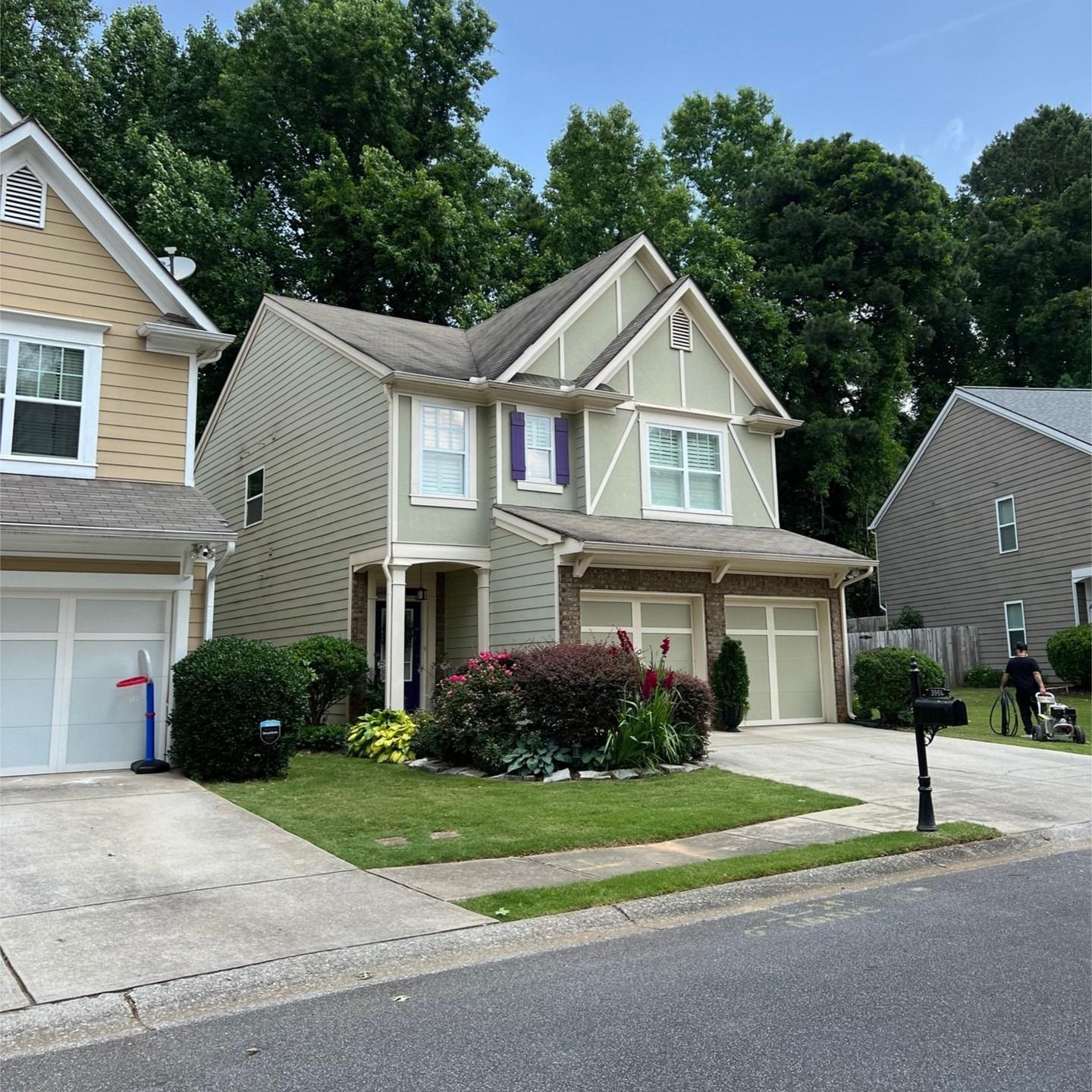 Light-green two-story suburban house with a tan-colored neighboring home and a shared concrete driveway.