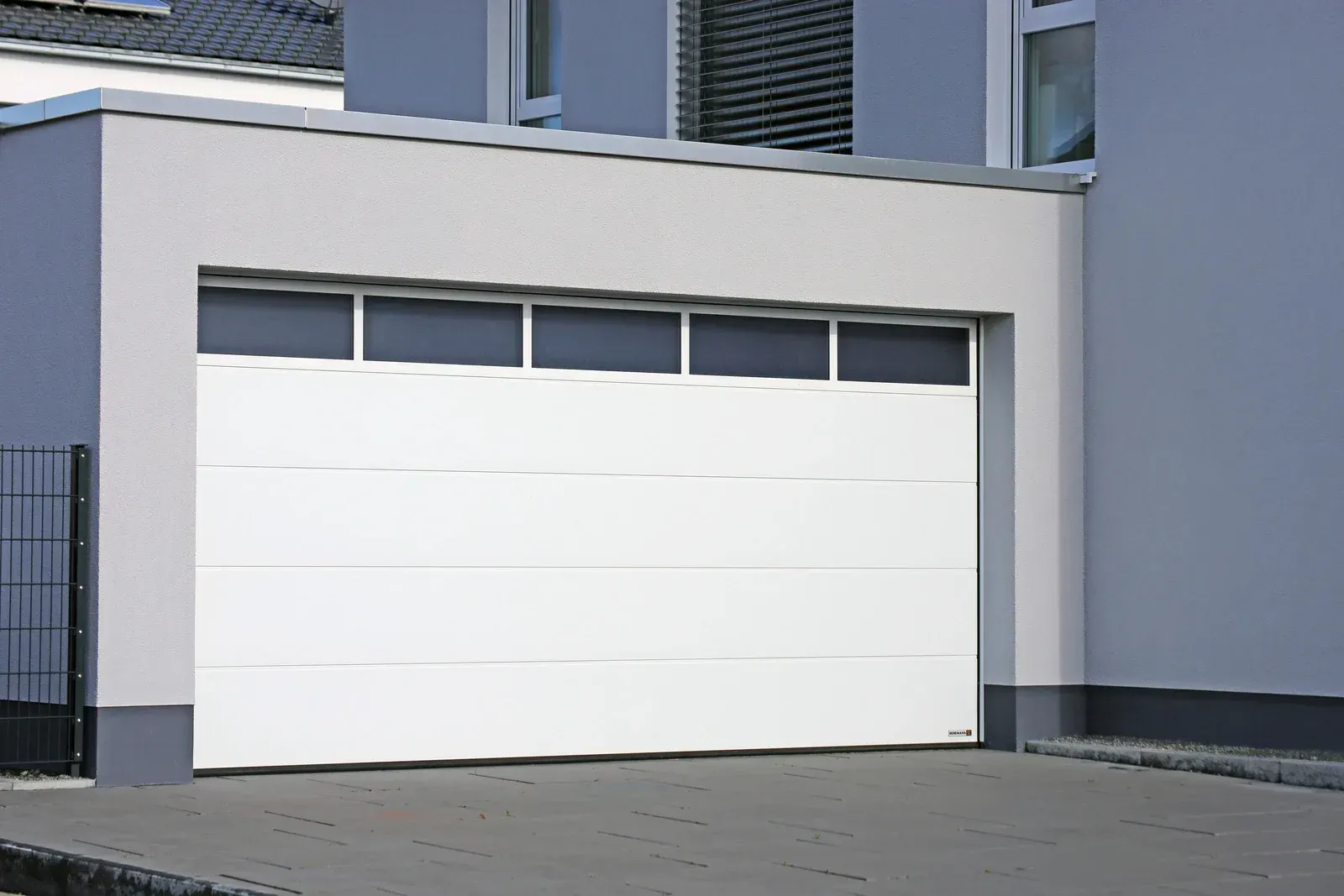 White garage door on a gray building with windows above the door.