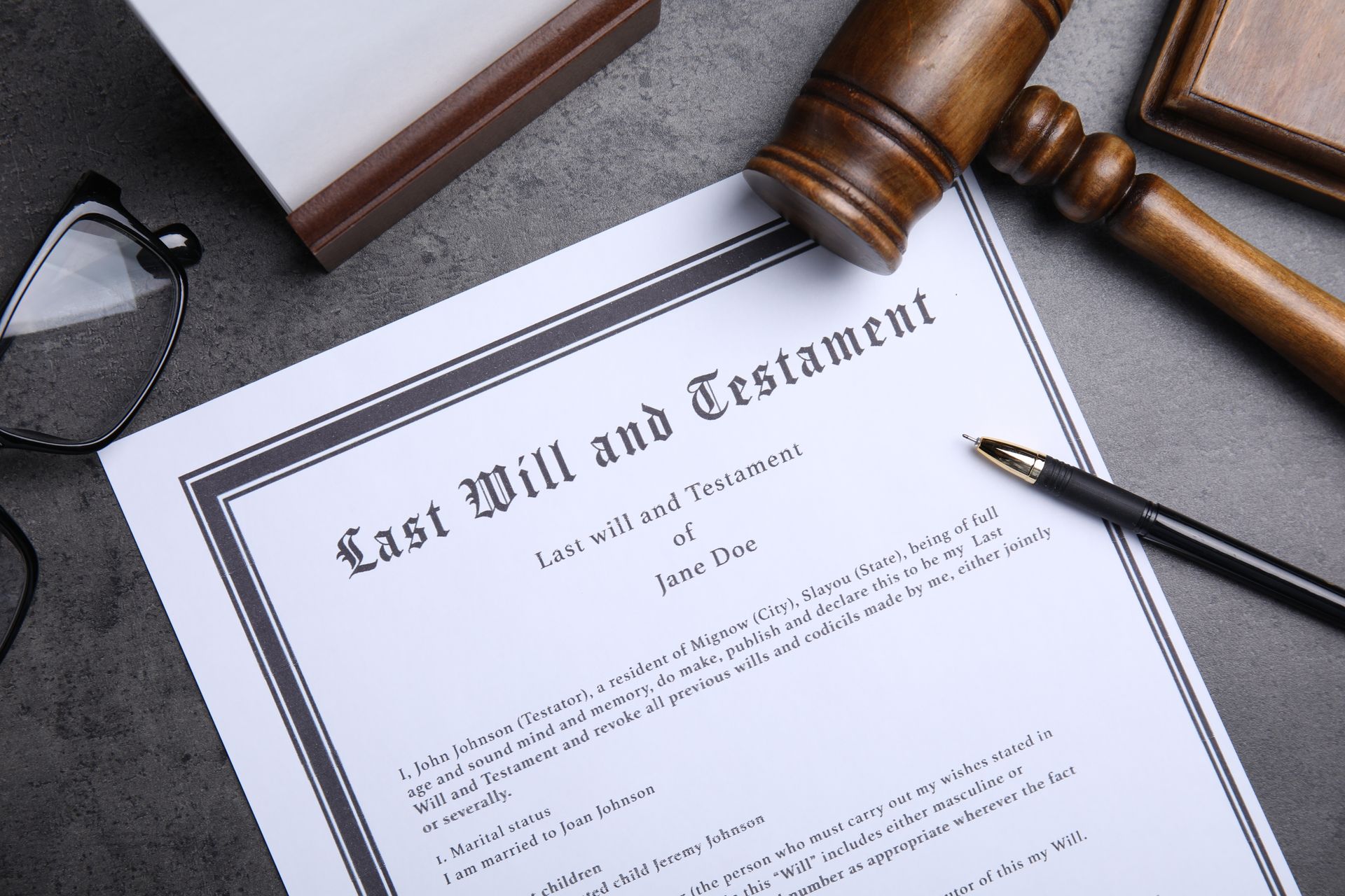 Will and testament document with gavel, pen, and glasses on a gray surface.