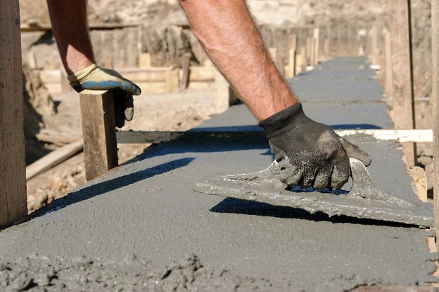 A man is spreading concrete on a sidewalk.