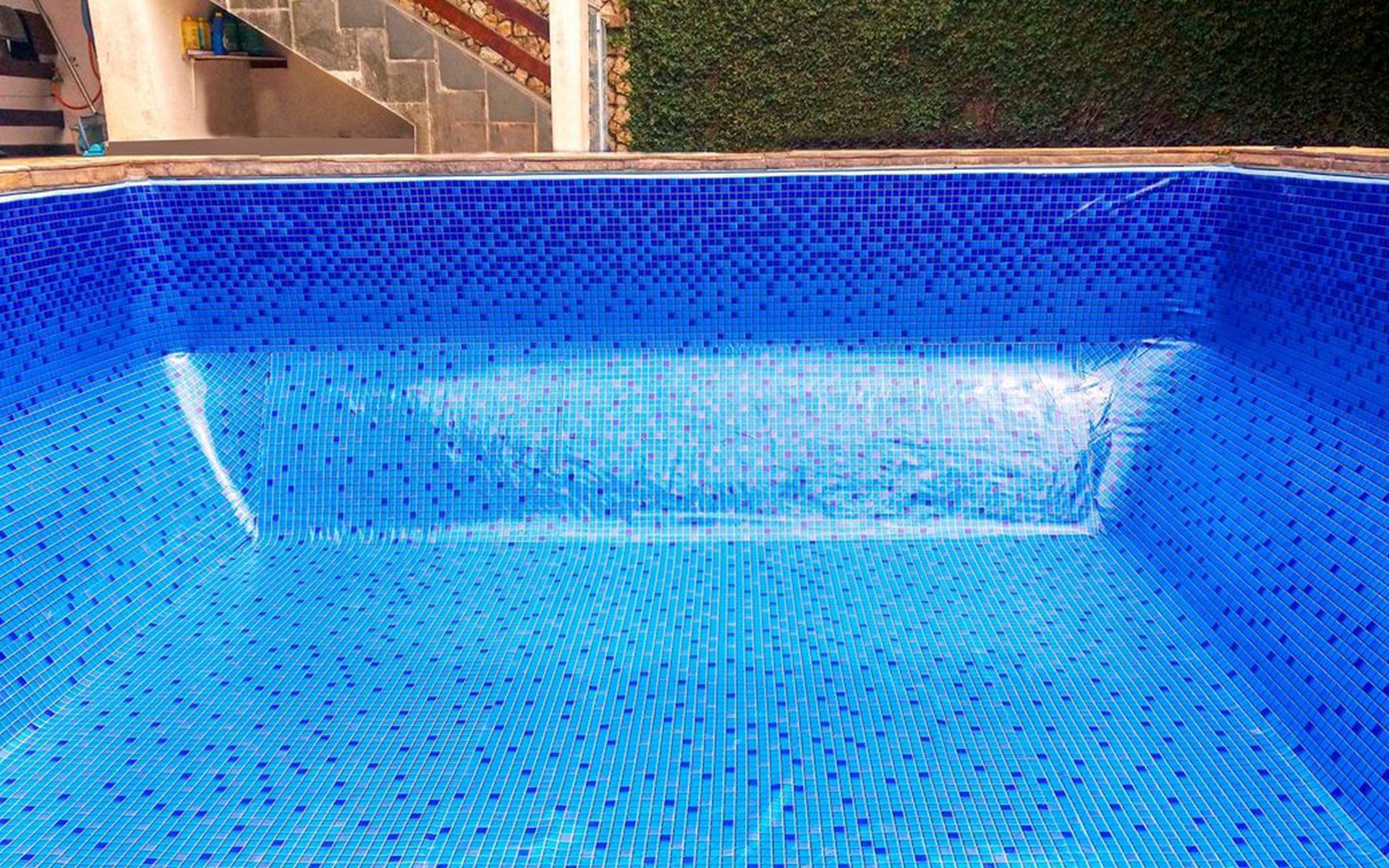 A blue swimming pool with a staircase in the background.