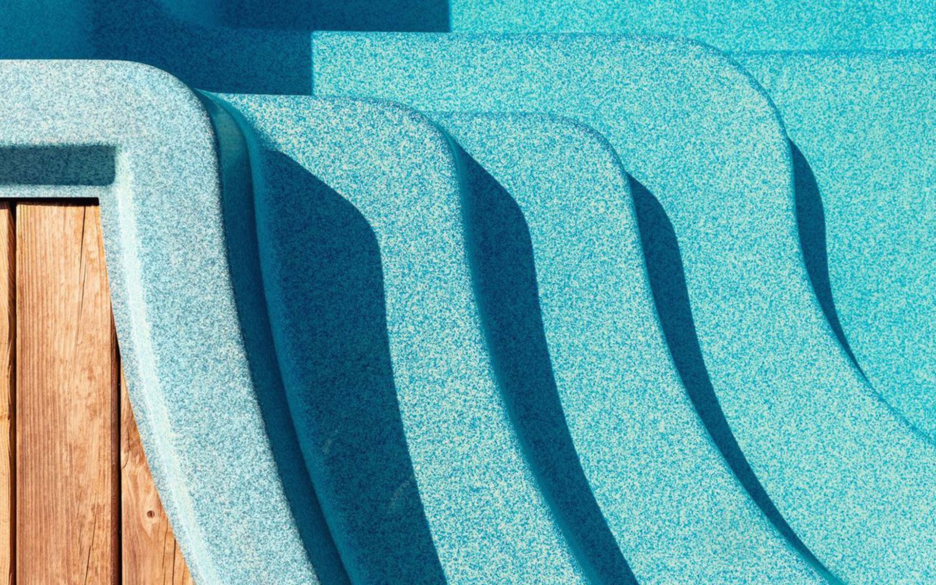A close up of a swimming pool with stairs and a wooden deck.