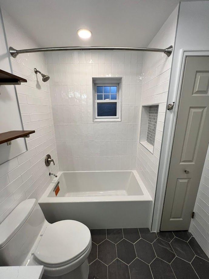 A bathroom with a toilet , tub , shower and window.