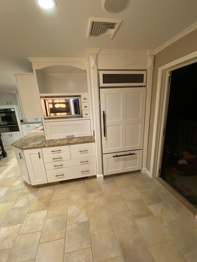 A kitchen with white cabinets , a refrigerator and a microwave.