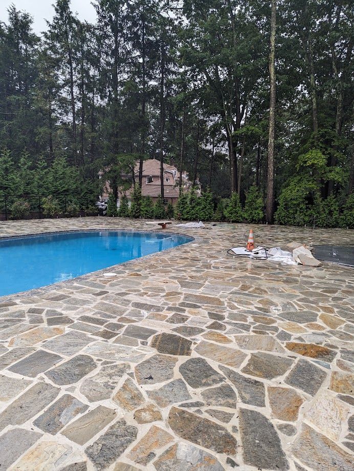 A large swimming pool surrounded by trees and a stone patio.