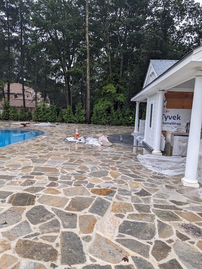 A stone patio with a pool in the background and a house in the background.