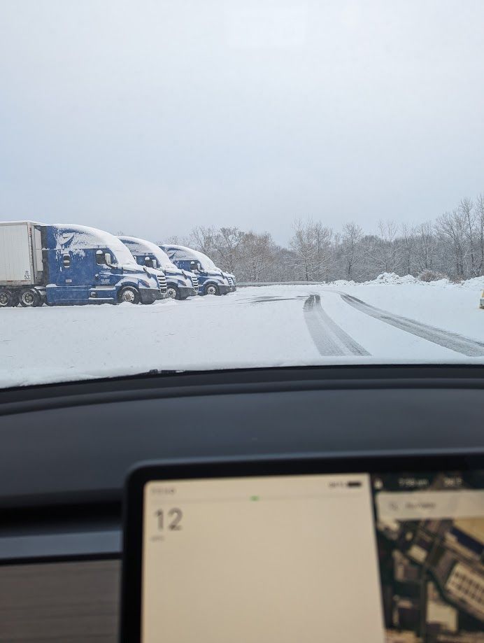 A row of trucks are parked in the snow on the side of the road.