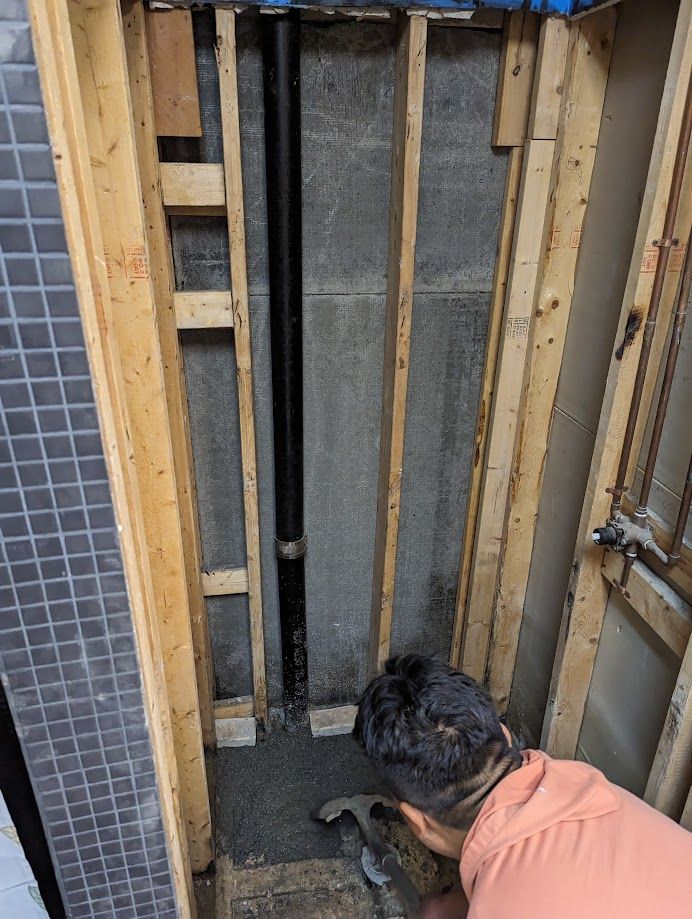 A man is working on a pipe in a bathroom.