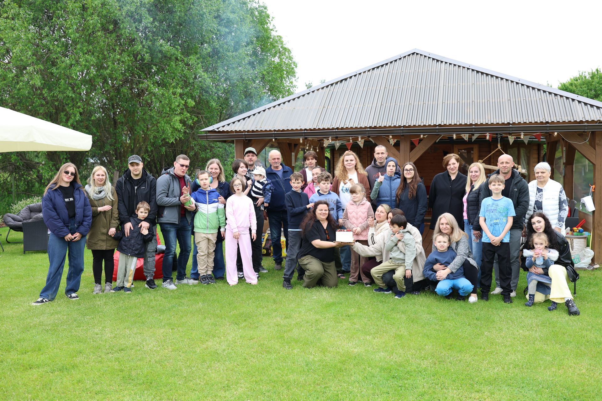 Group of people posing together on a lawn in front of a pavilion, with a tent at left.