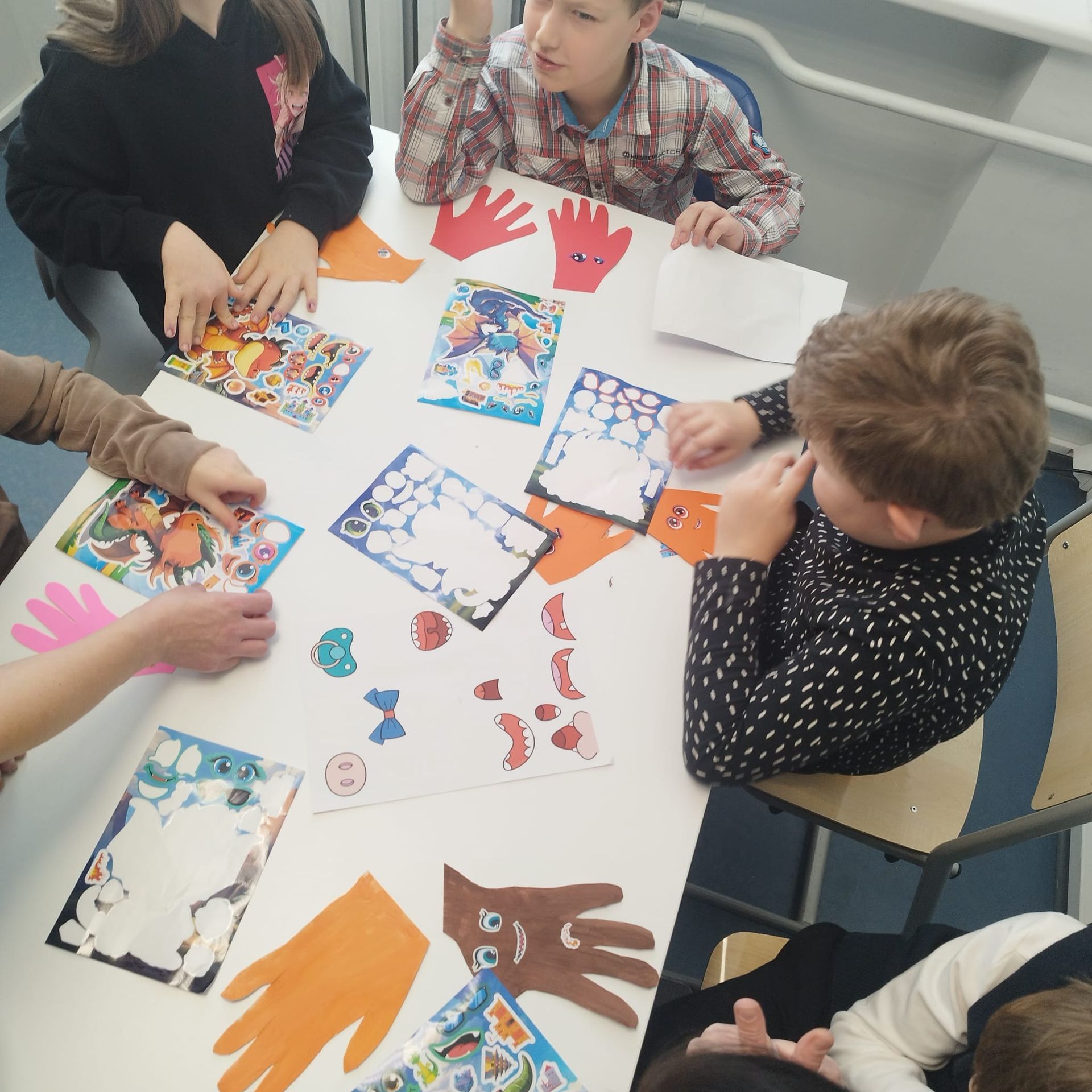 Children at a table making art; colored hand cutouts, paper, and art supplies.