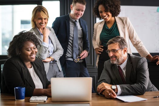 A group of business people are sitting around a table looking at a laptop computer.