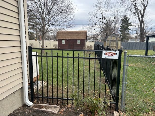 A black fence with a caution sign on it is in front of a house.