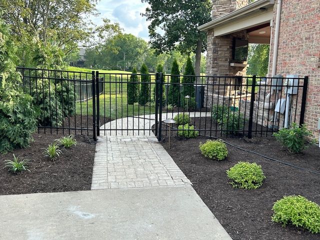 A metal fence surrounds a walkway leading to a house.