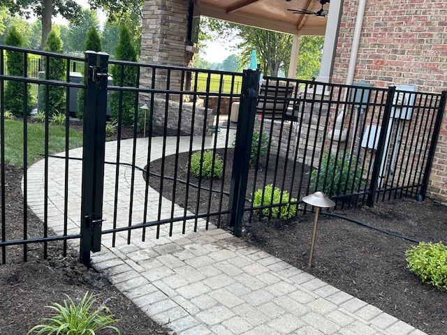 A black fence surrounds a brick walkway in front of a brick house.