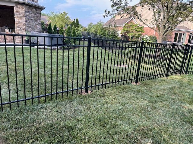A black metal fence surrounds a lush green lawn in a backyard.