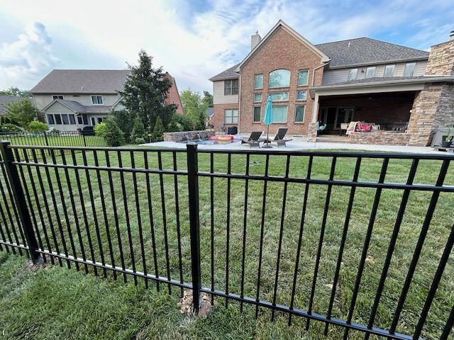 A black fence surrounds a large brick house in a backyard.
