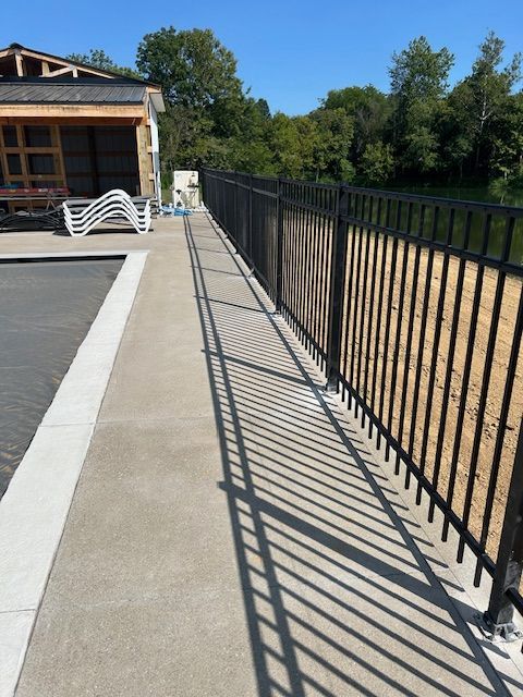 A fence along a sidewalk with a pool in the background