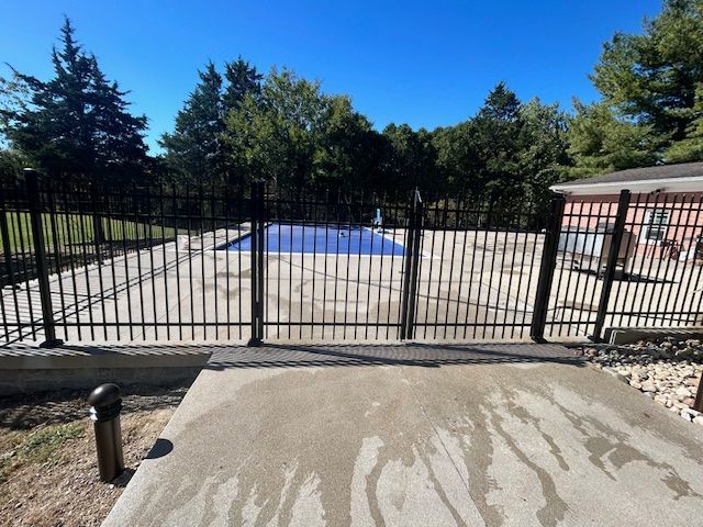 A fence surrounds a swimming pool with trees in the background