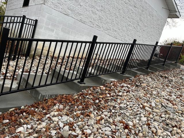A black fence is surrounded by rocks and leaves in front of a white building.