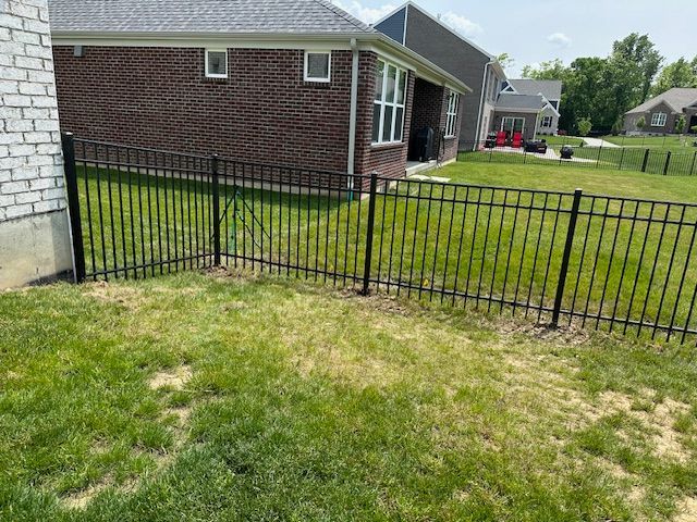 A black fence surrounds a lush green yard in front of a brick house.