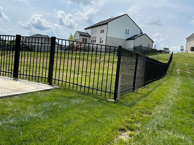 A black fence surrounds a lush green field in front of a house.