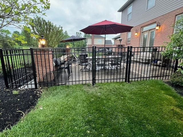 A fence surrounds a patio with tables and chairs and a red umbrella.