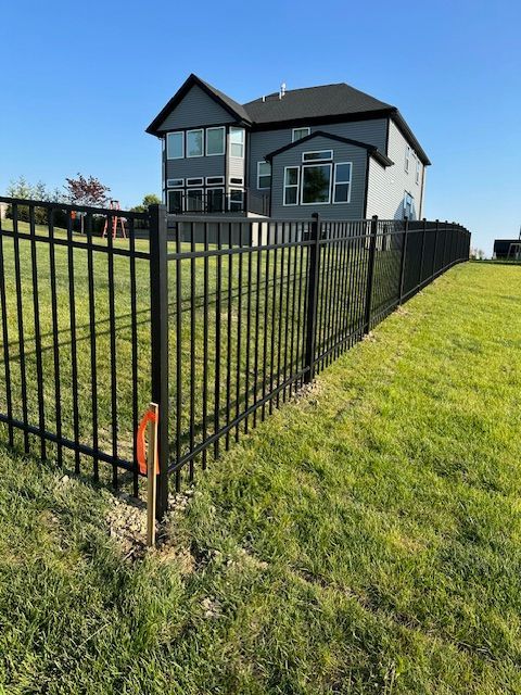 A black fence surrounds a lush green field in front of a house.