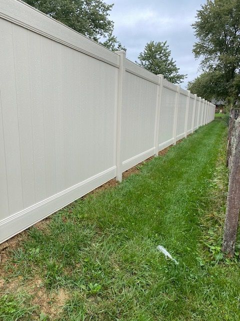 A white vinyl fence is sitting in the middle of a lush green field.