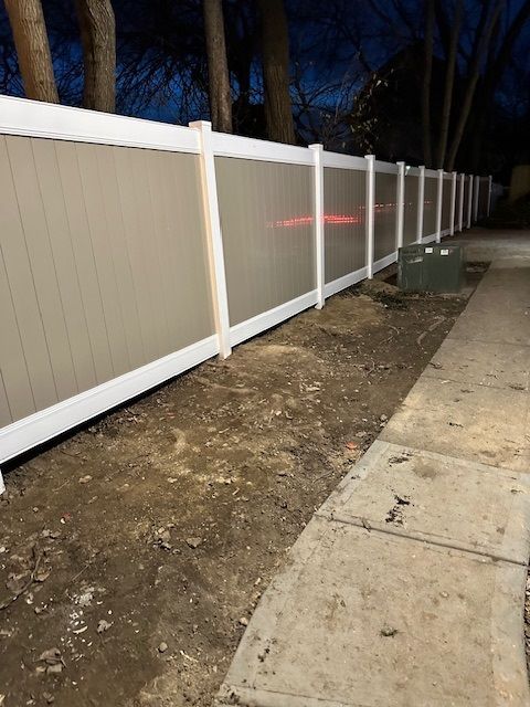 A white fence is sitting next to a sidewalk.