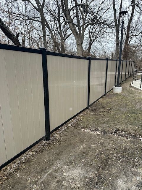 A white fence with black trim is surrounded by trees and dirt.