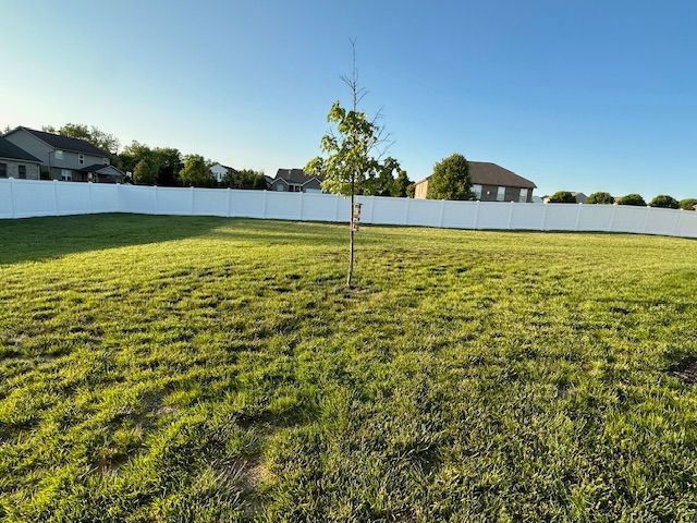 A white fence surrounds a lush green field with a tree in the middle.