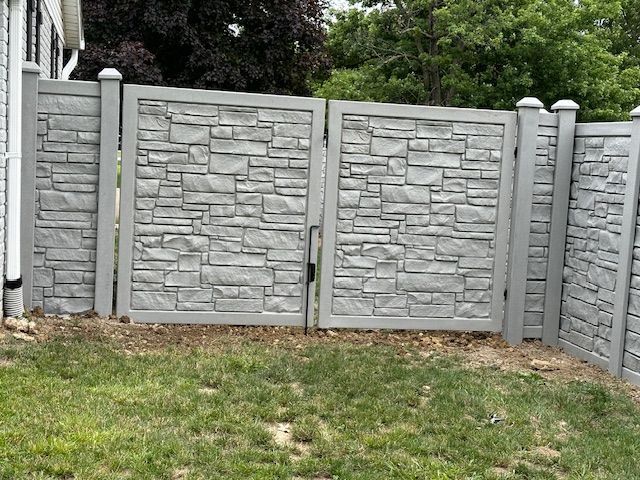 A stone fence with a gate in the backyard of a house.