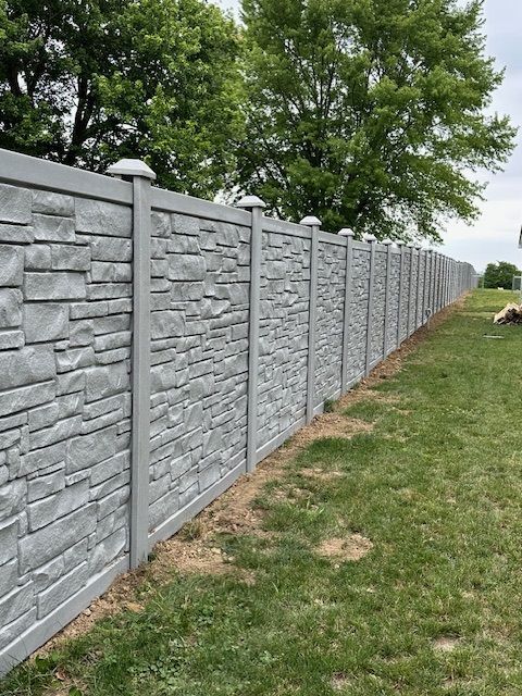 A long stone fence is surrounded by grass and trees.