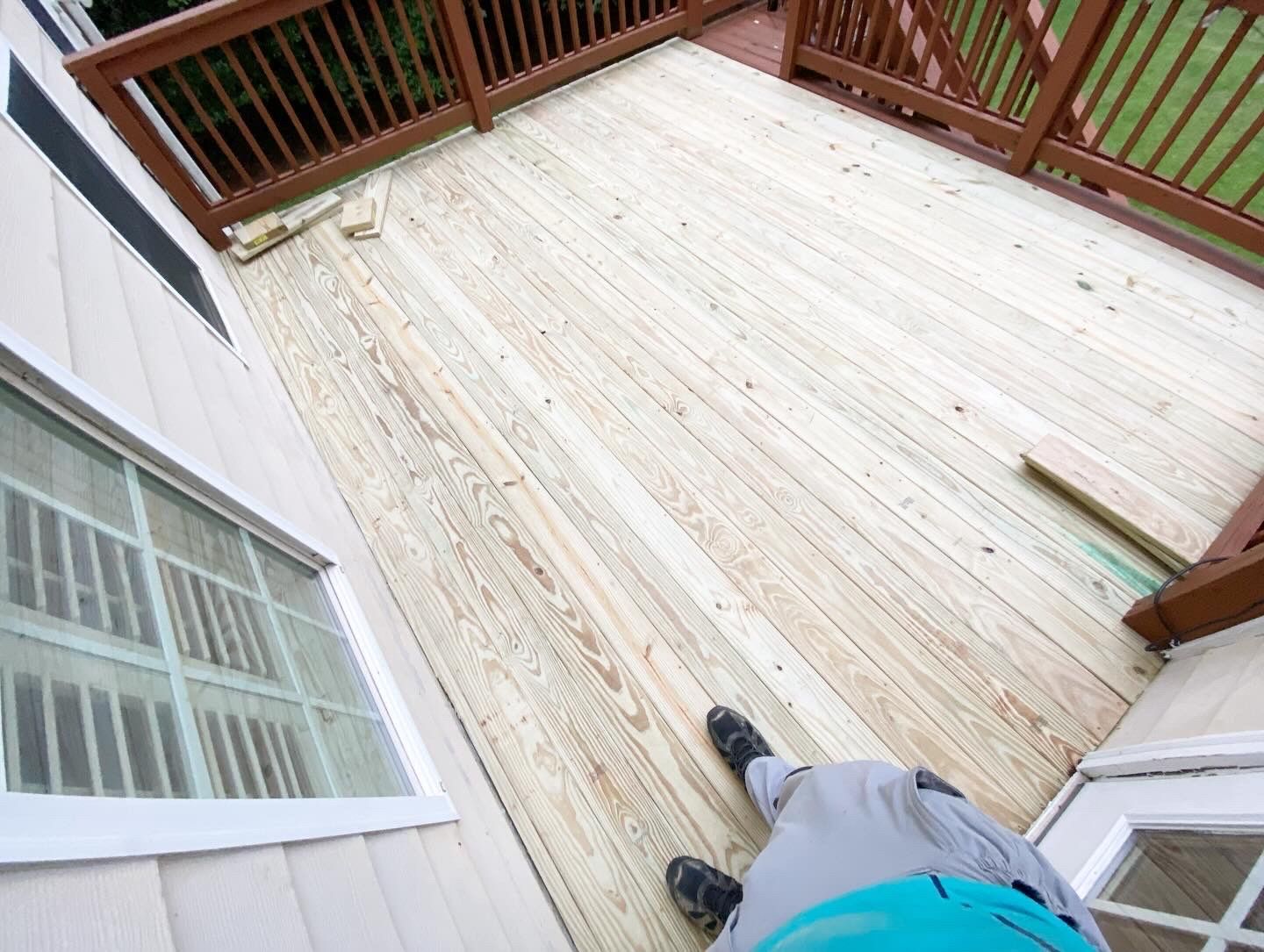 Wooden deck with brown railing, next to a light-colored house. A person stands on the deck.