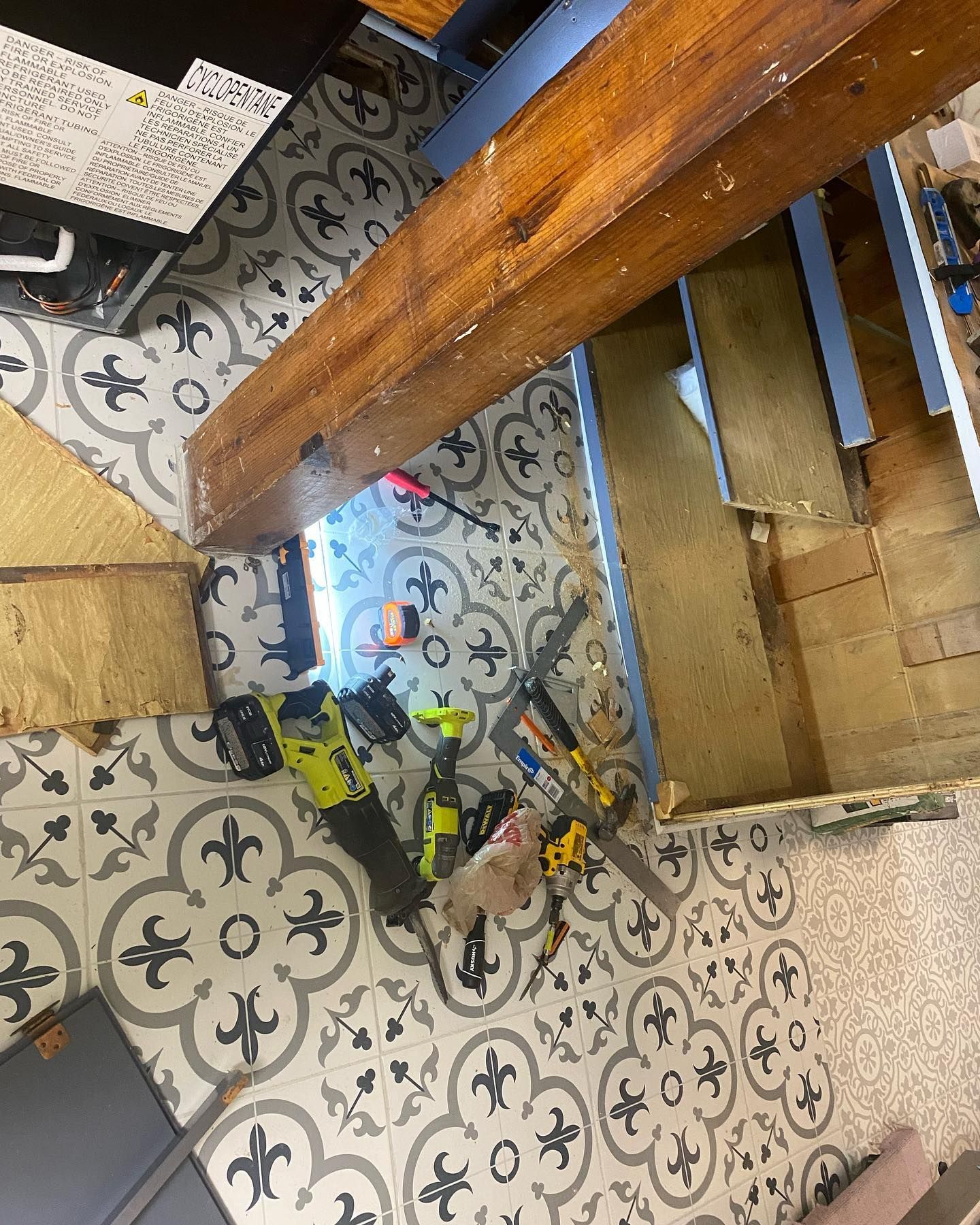 Tools on a patterned tile floor under a wooden beam during construction.
