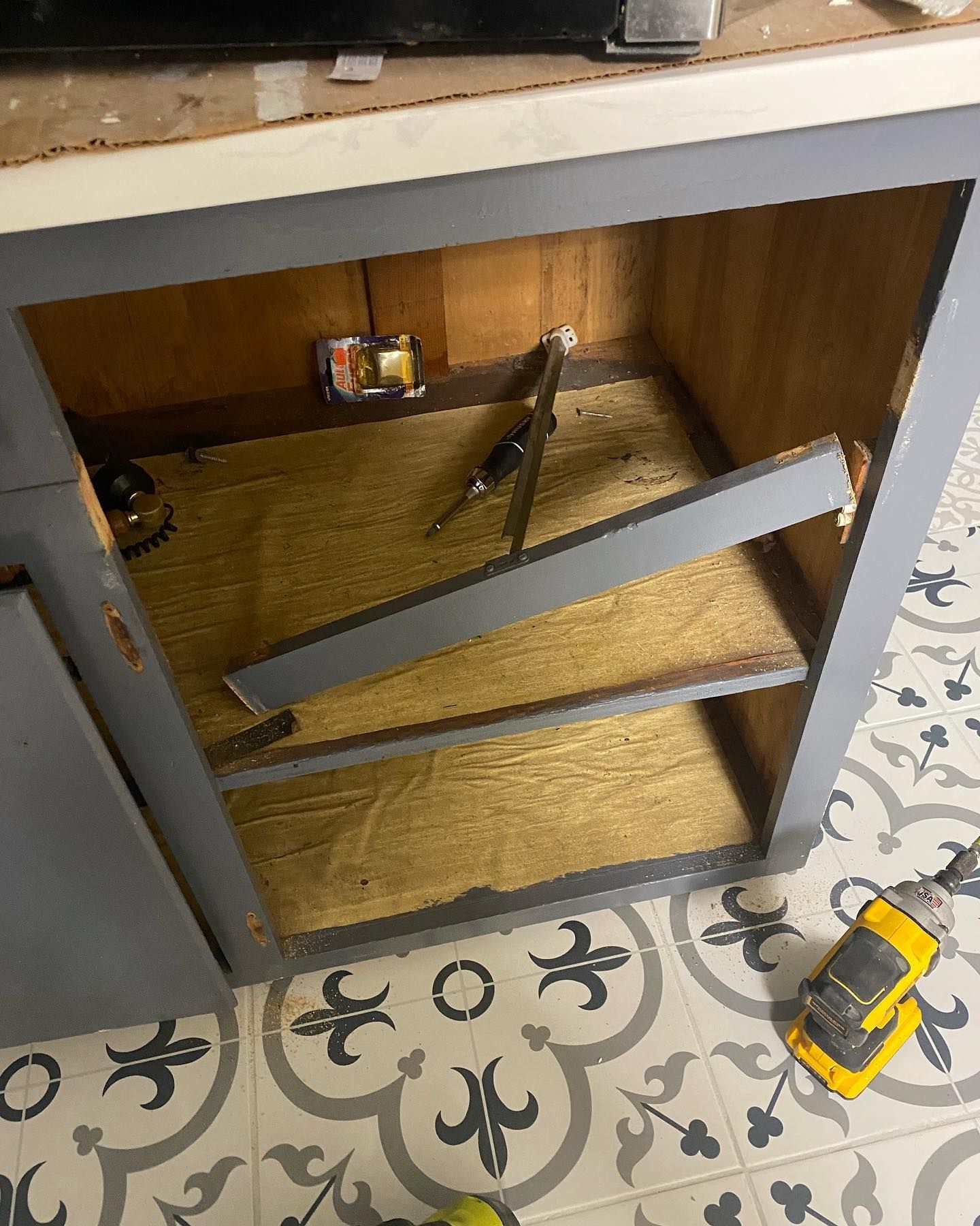 Open kitchen cabinet with broken shelf and exposed interior, paint colors gray, brown, and white.