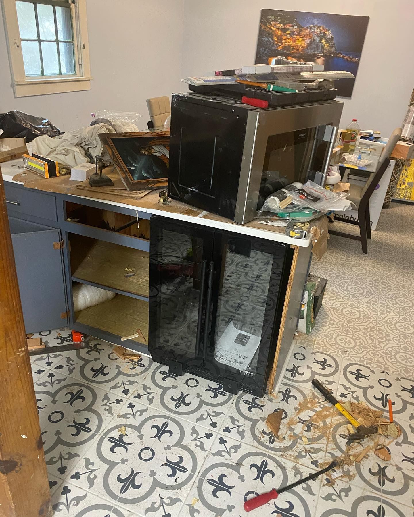 Cluttered room with a broken wine cooler on a workbench and tools on the floor.