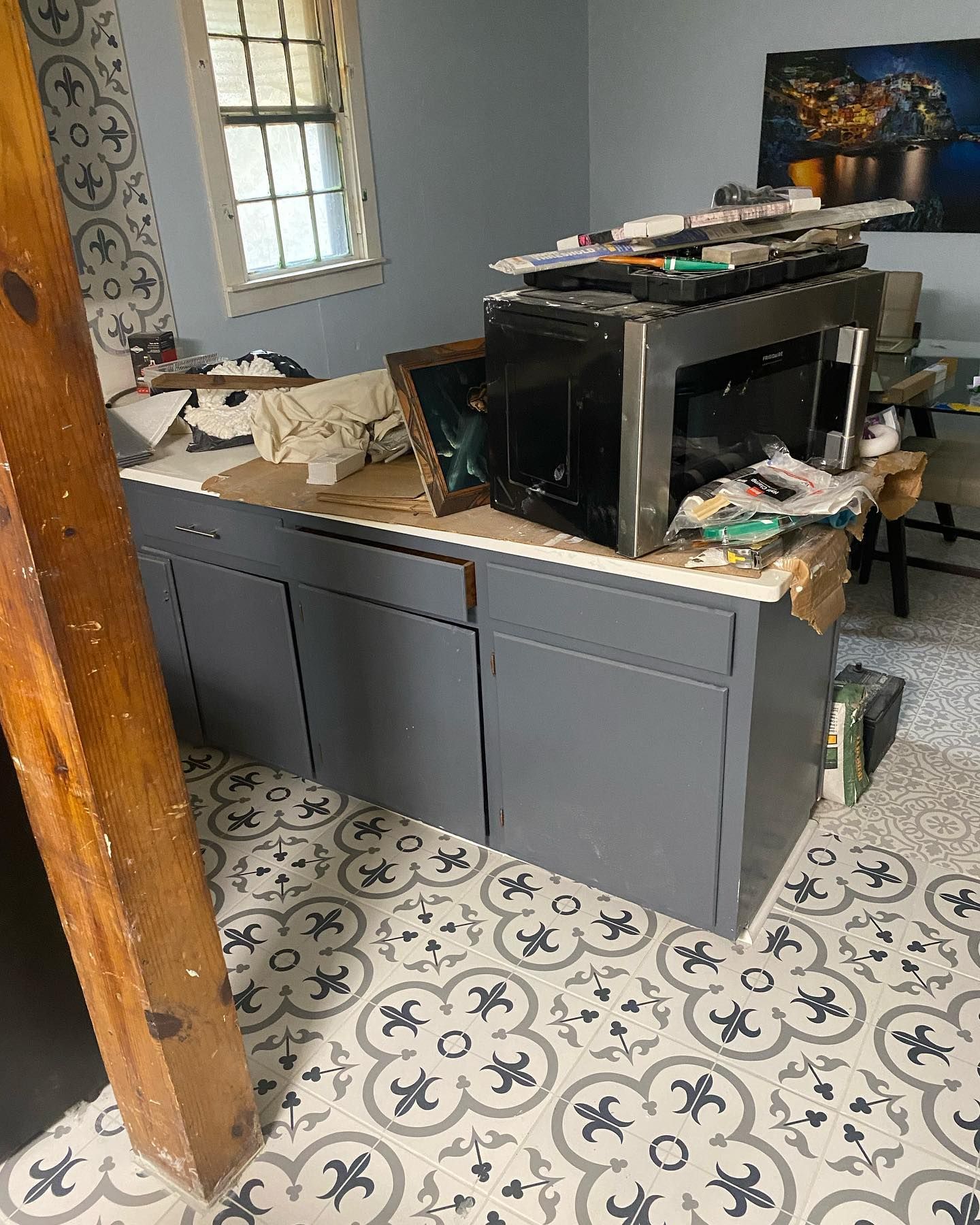 Grey cabinet with clutter on top, patterned floor, window.