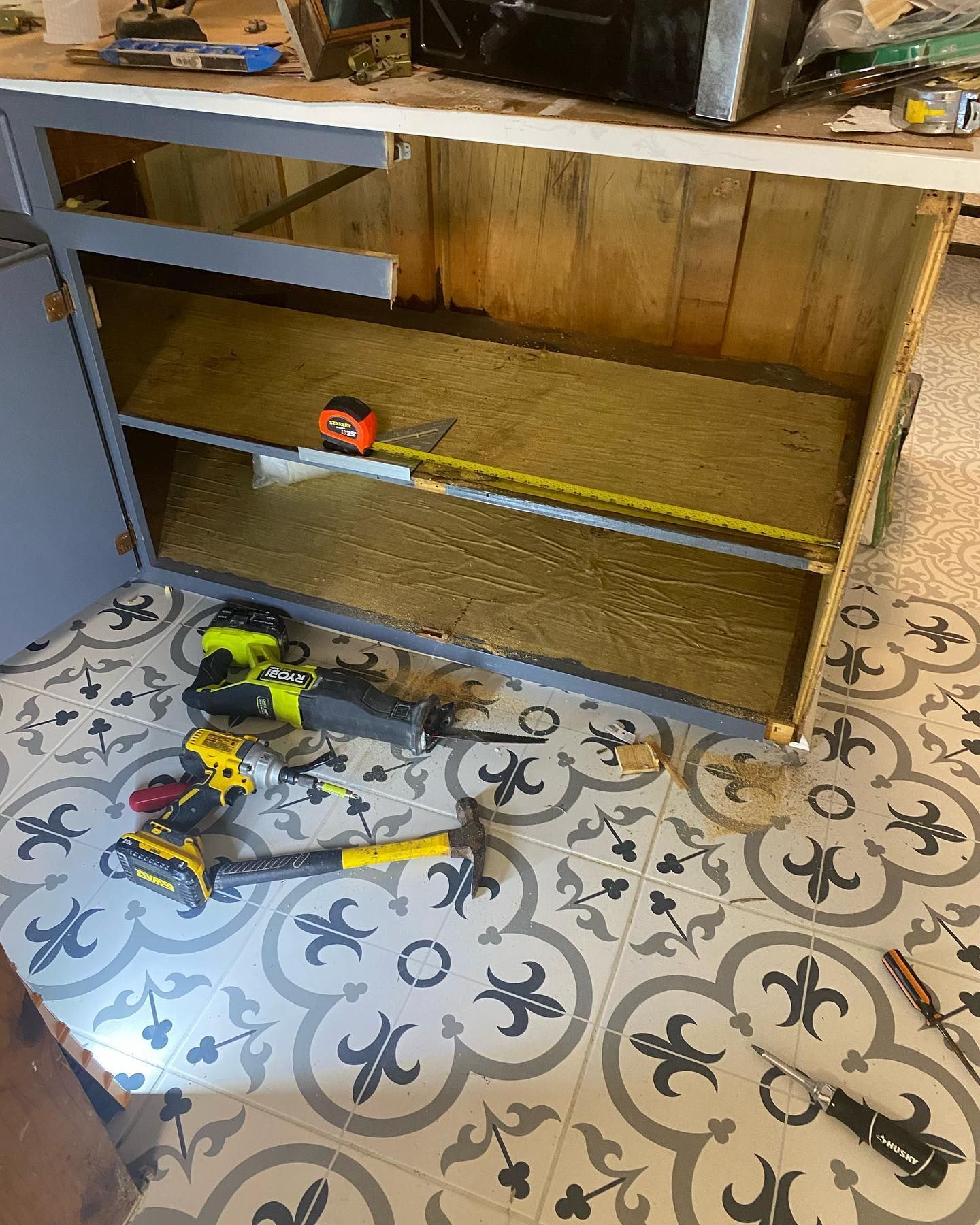 Cabinet interior under renovation, with tools on patterned tile floor.