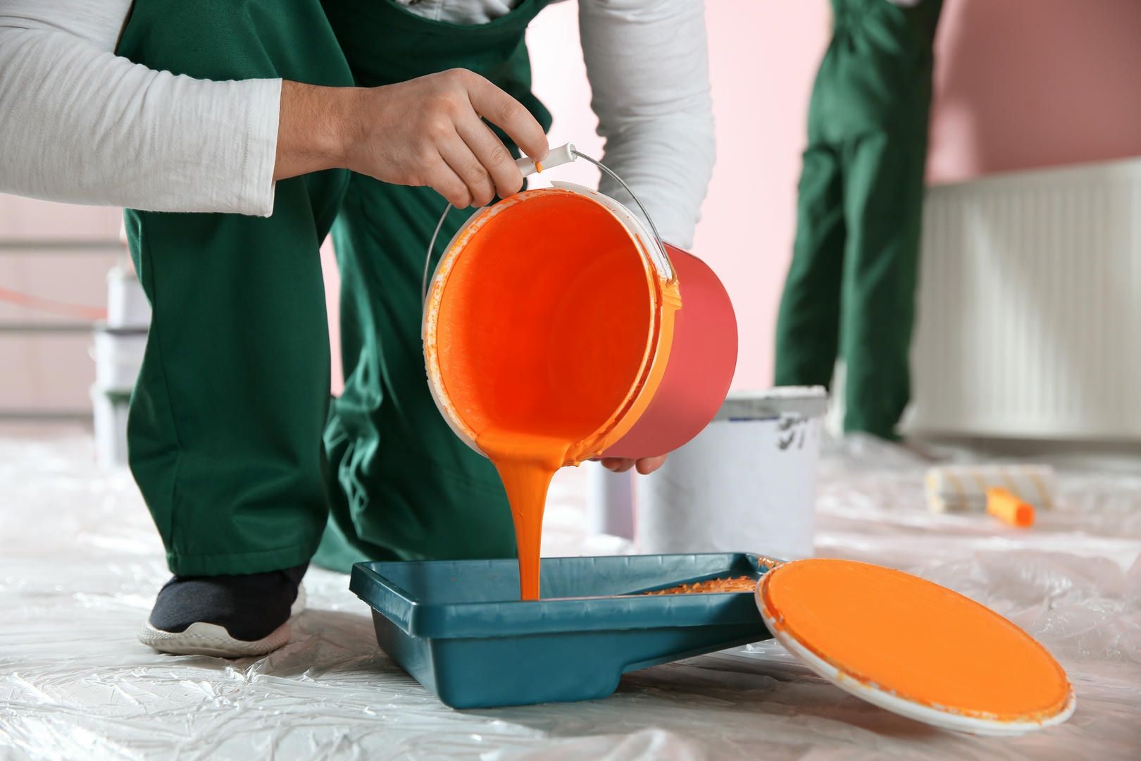 Person pouring orange paint into a tray, preparing to paint a room.