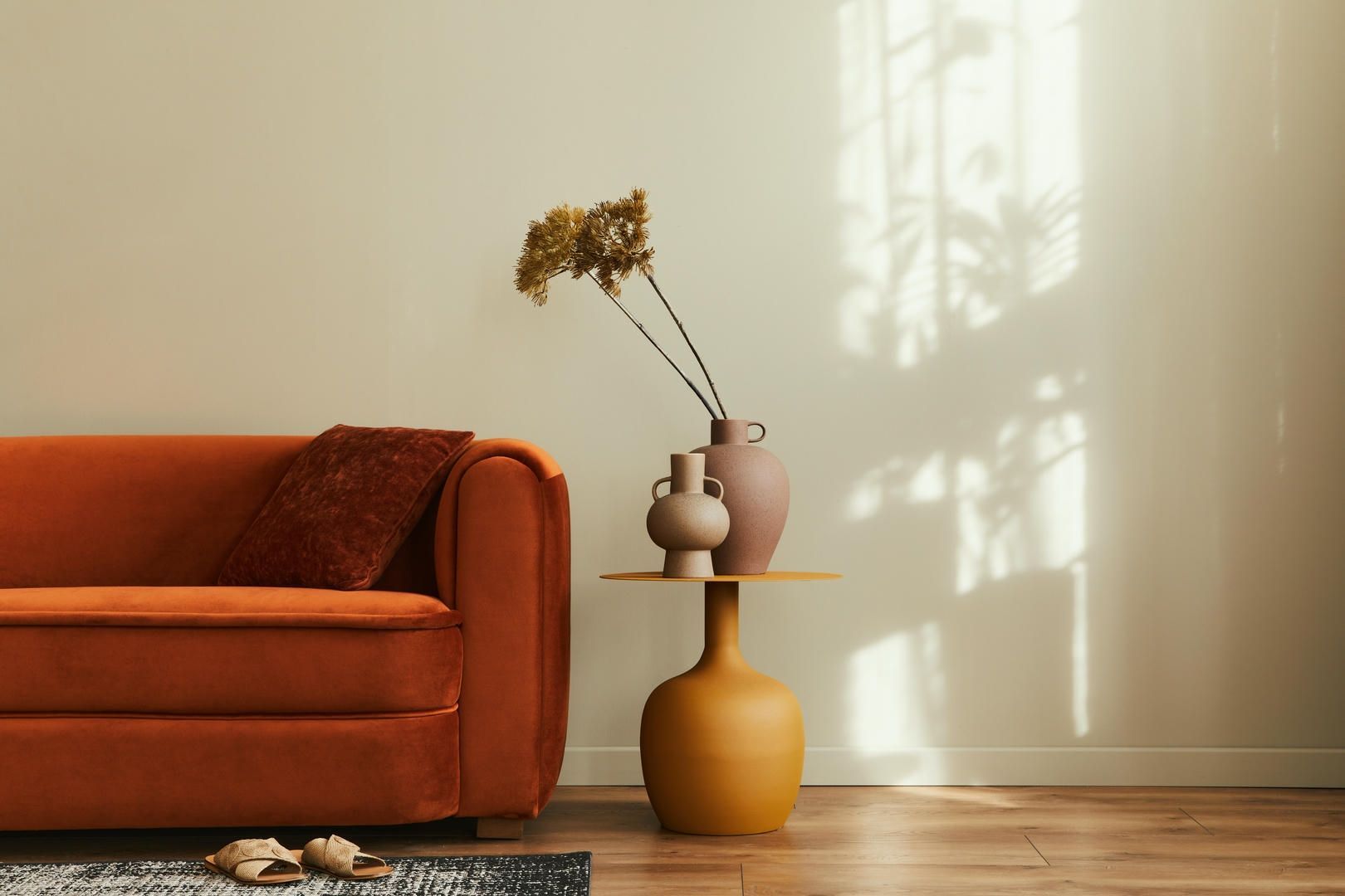 Orange velvet couch beside a yellow table with vases of flowers, in a room with light-colored walls.