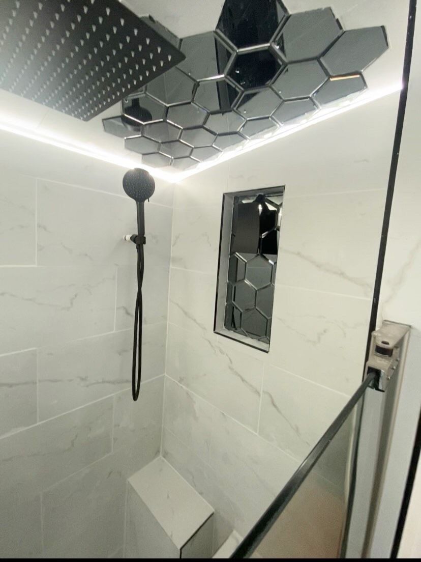 Modern shower with white tiles, black fixtures, and a hexagon-tiled ceiling and niche.