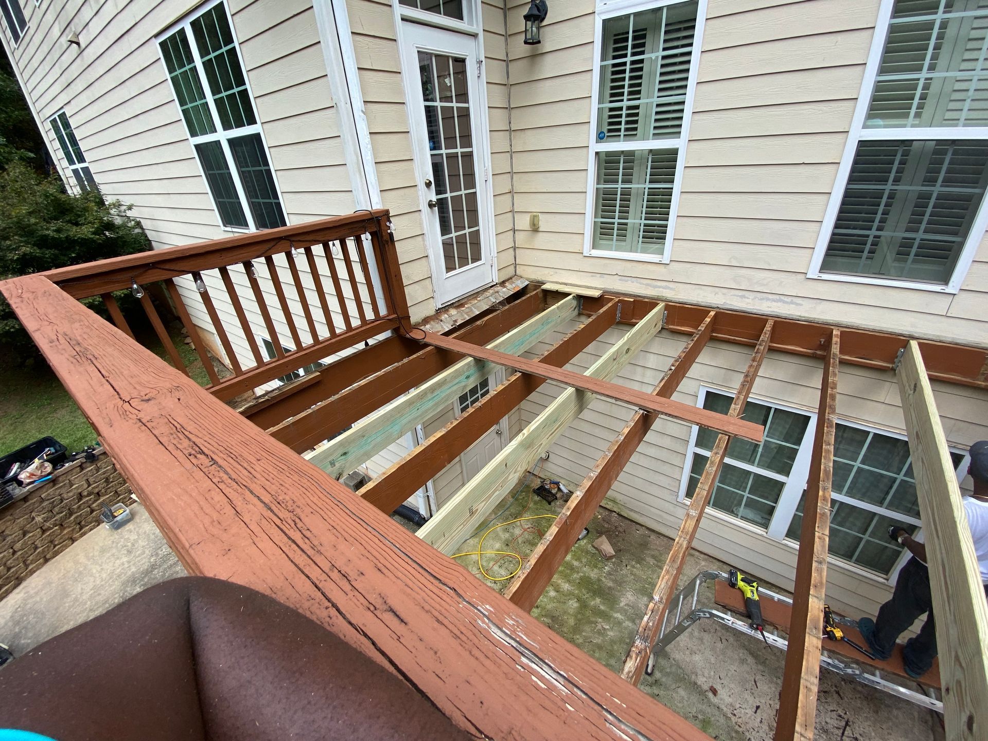 Deck under construction; wooden beams and railing against a house with windows.