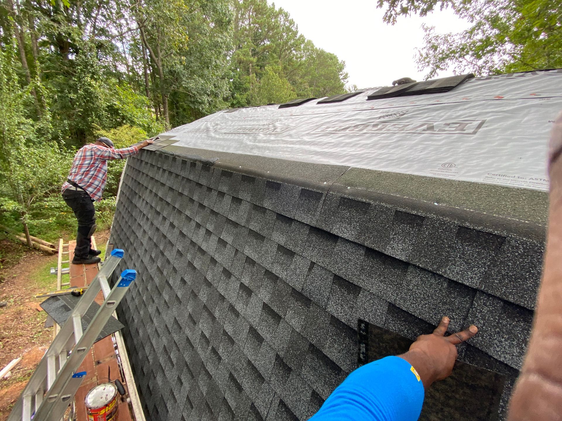 Roofer on a rooftop, installing dark gray tiles against a blue sky.