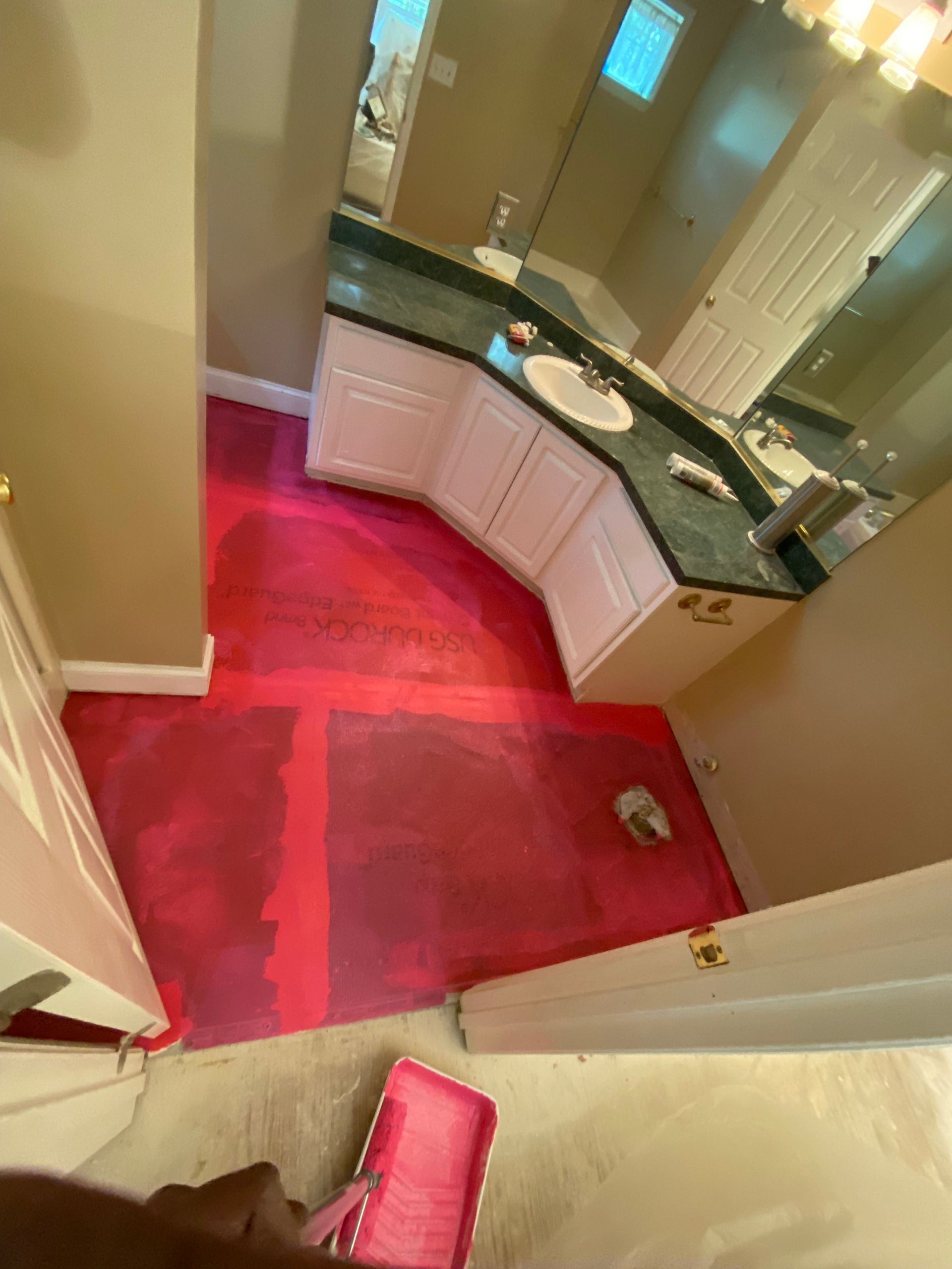Bathroom with hot pink painted floor; white cabinets, green countertop.