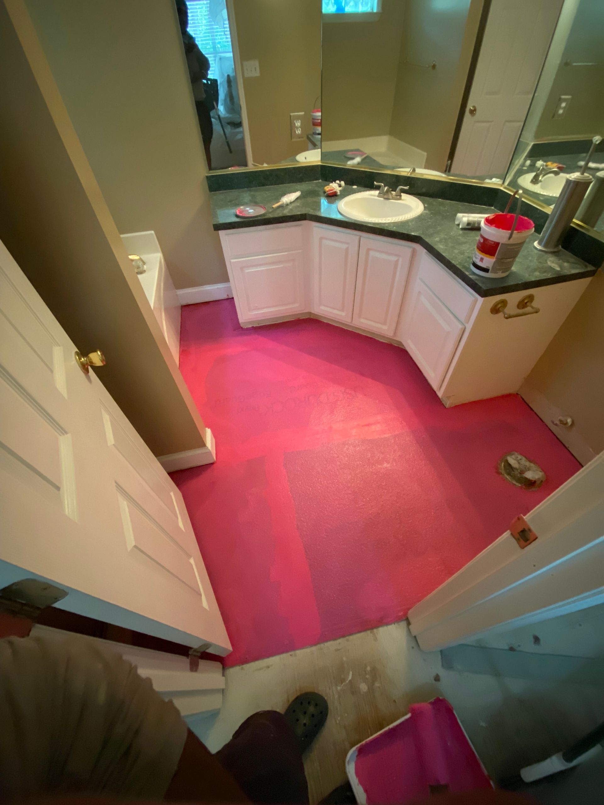 Pink painted bathroom floor. White cabinets, green countertop, and a partly open door are visible.
